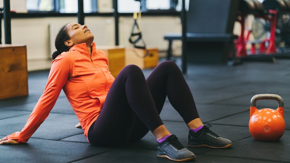 Woman sits next to kettlebell in gym