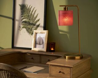 brass desk light with pink shade against a green wall and wooden desk