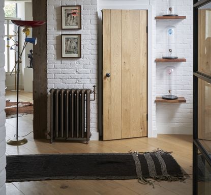 Hallway with wood flooring, white brick walls, large metal radiator and black rug on the floor