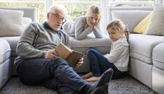 A grandfather and his two granddaughters read on a couch.