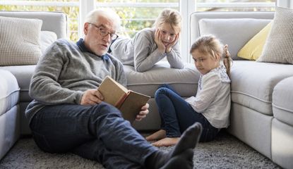A grandfather and his two granddaughters read on a couch.