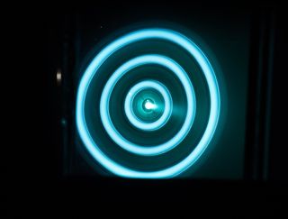 A head-on shot of the X3 ion thruster firing at 50 kilowatts, viewed through a warped mirror in the vacuum chamber.