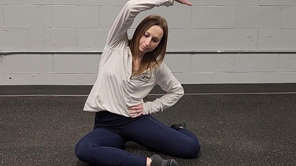 Woman demonstrating stretch. She wears a white long-sleeve top, blue sports leggings and black socks
