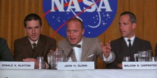 three men in suits sit at a table with the NASA logo behind them