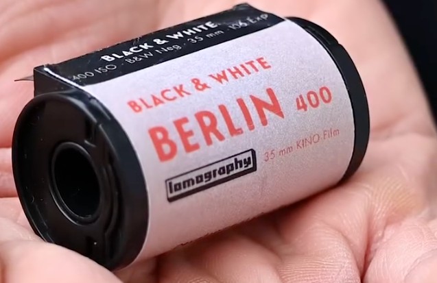 A person's hand holds a roll of Lomography Berlin 400 Black &amp; White 35mm film, which is uniquely labeled for 106 exposures.