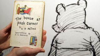 Person holding up a copy of 'The House of Pooh Corner' next to an illustration of Winnie the Pooh