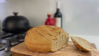 A loaf of bread cooked in the Le Creuset Cast Iron Bread Oven, with the Le Creuset Cast Iron Bread Oven in the background