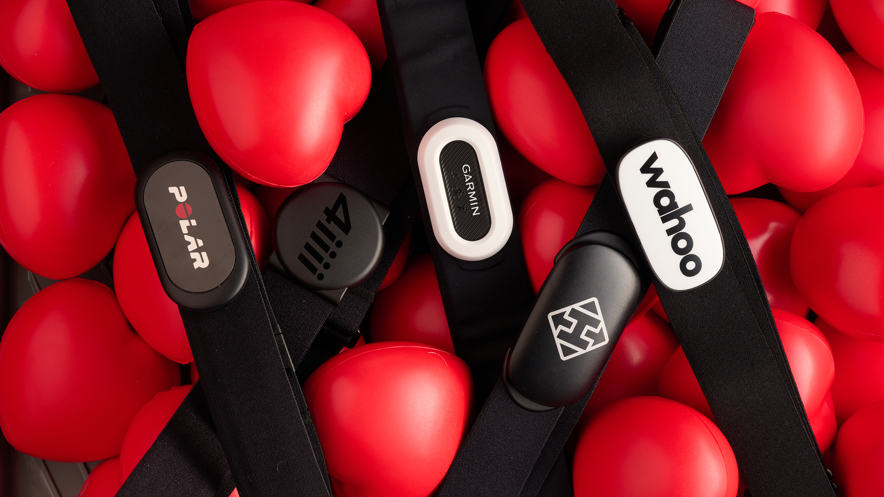 5 of the best heart rate monitors set to the background of some little red soft heart shaped stressballs. 