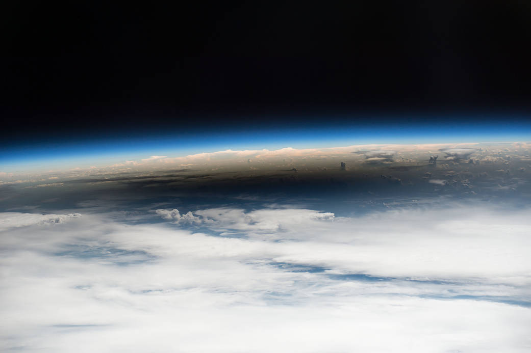 A large dark solar eclipse shadow appears over the cloud tops of Earth as viewed from space.