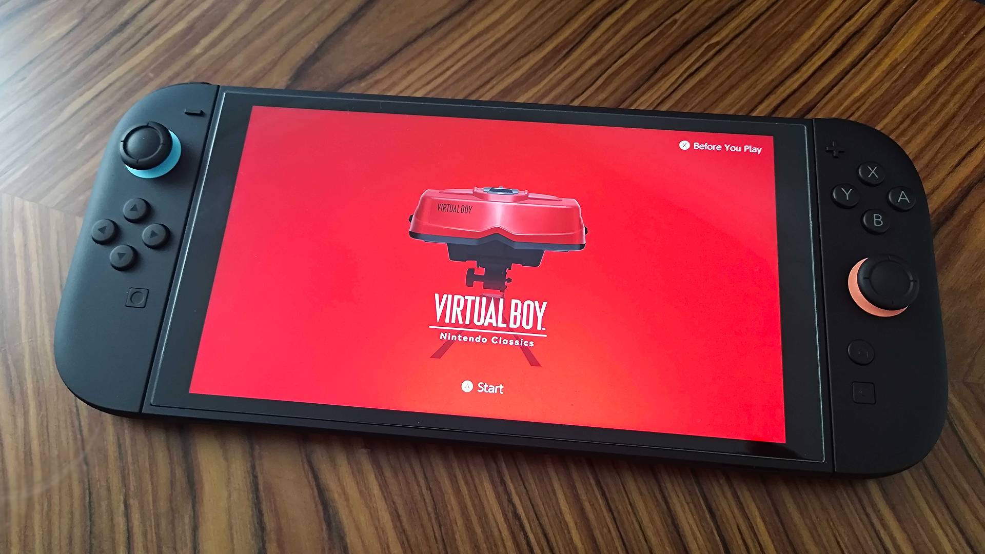 Nintendo Switch 2 on woodgrain table with red Virtual Boy app intro screen displayed.