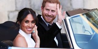 Meghan Markle and Prince Harry wave from inside a convertible car.