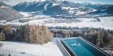 An infinity pool overlooks a snowy valley in the sunshine as a woman swims towards its very end.