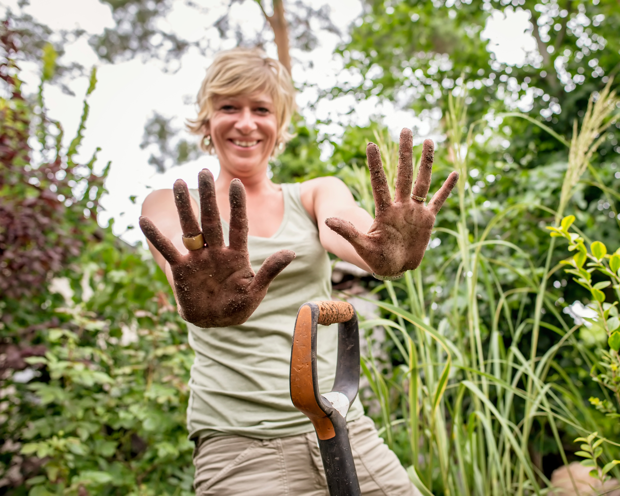 smiling woman showing soil covered hands to camera in garden