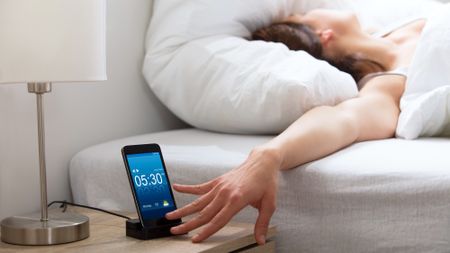 woman next to alarm clock on phone in bed