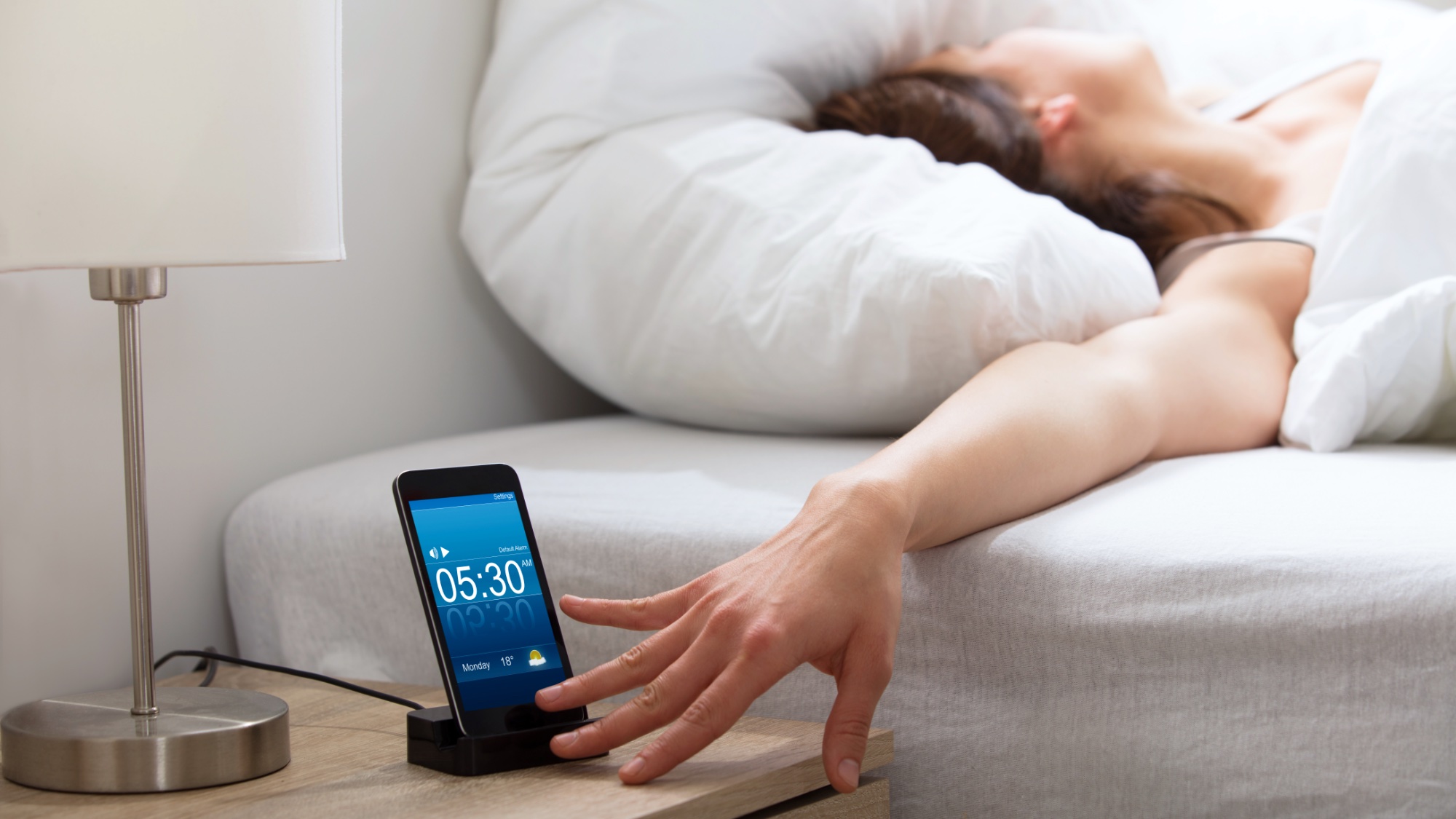 woman next to alarm clock on phone in bed