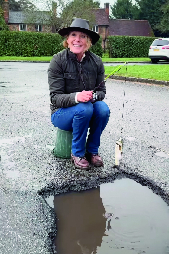 The motoring journalist Julia Roberts pretends to fish in a giant waterfilled pothole.