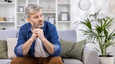 An older man sitting on his sofa looks concerned.