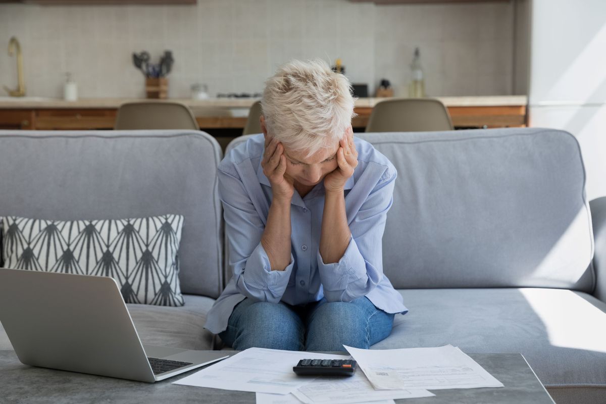 An elderly woman looking concerned looking at a calculator and laptop