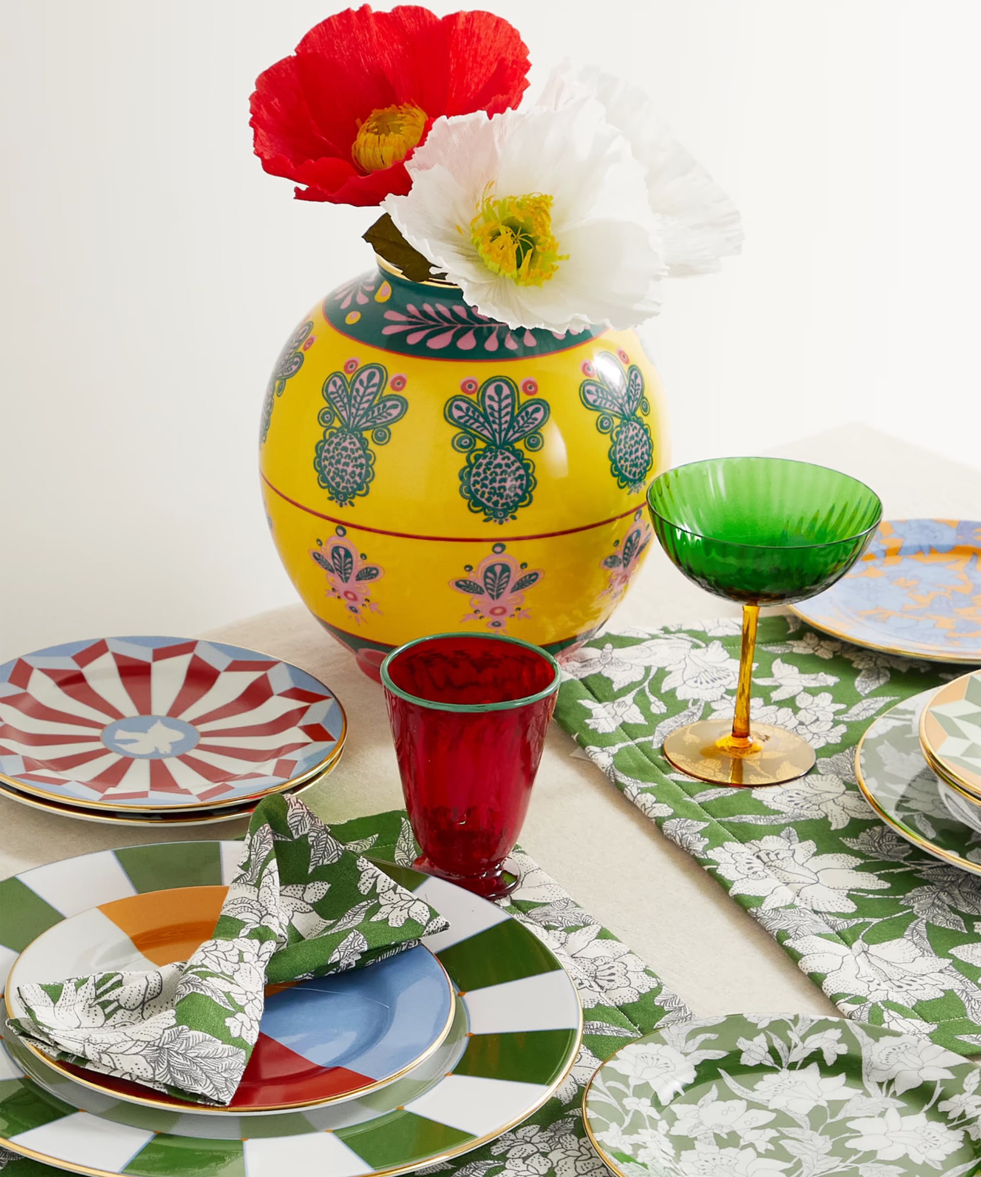 Green and white floral placemats with matching napkins and side plates, plus red and green glassware and a yellow and blue vase