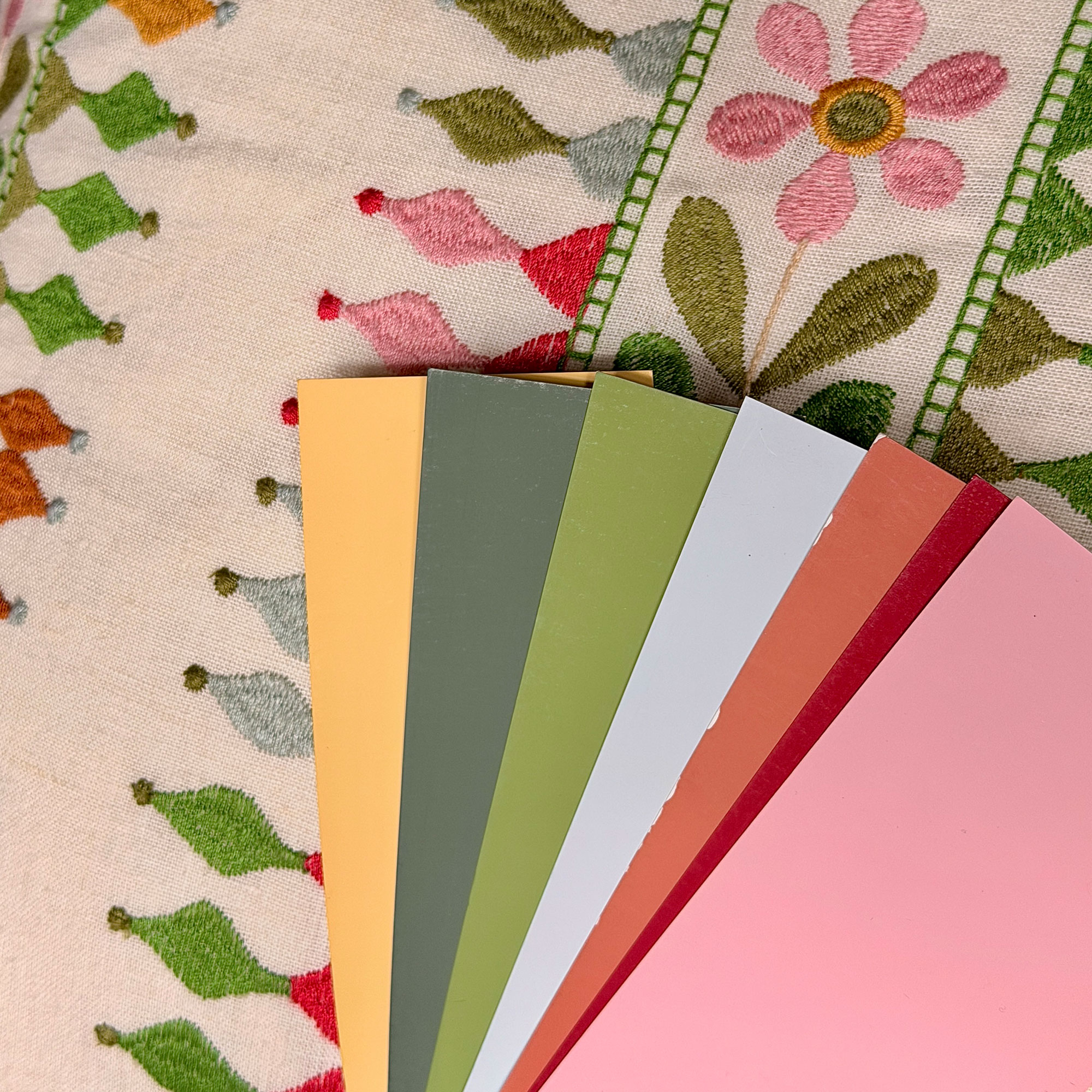 Paint sample cards fanned out above colourful embroidered fabric