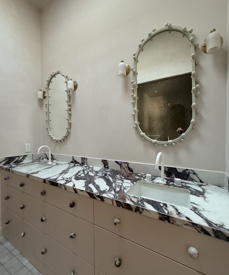 marble-topped bathroom vanity with two oval mirrors on the wall above it