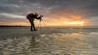 best travel tripods - photographer on a beach at sunset