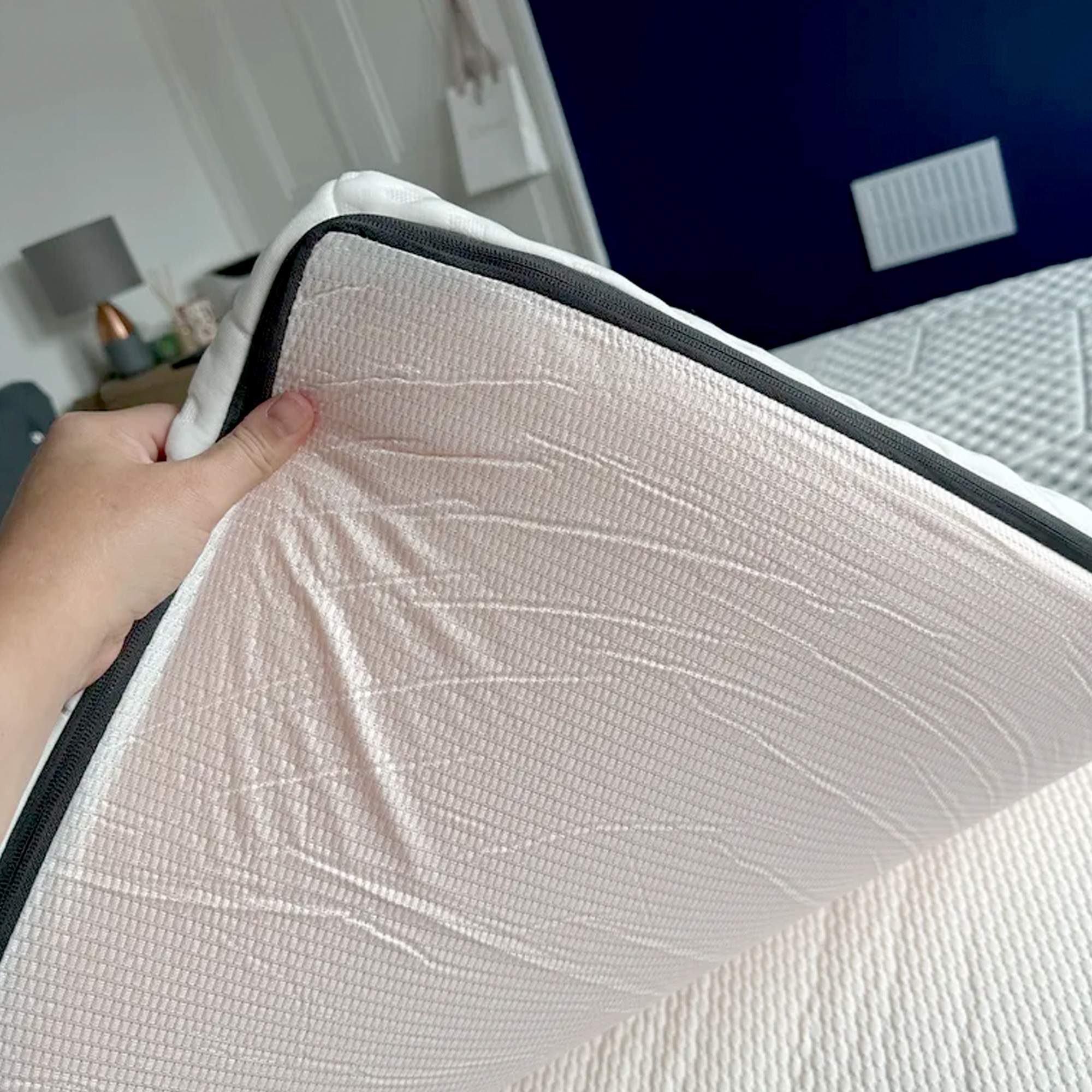 A hand turning over the edge of the Emma Premium mattress topper to show its anti-slip base