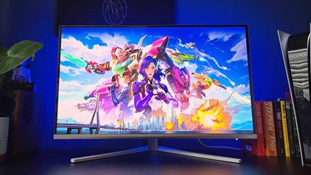 Philips Evnia 32M2N8900 monitor on black desk with ambilights illuminating back wall and Overwatch artwork on screen.