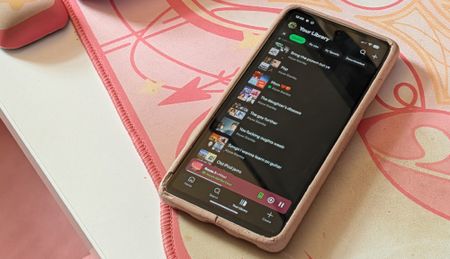 A picture of a Pixel 7a with the Spotify app pulled up on a pink desk mat. 