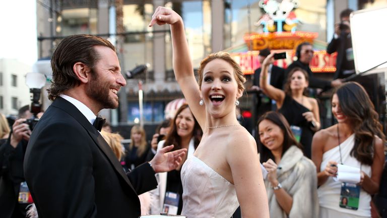 Jennifer Lawrence points playfully at Bradley Cooper on the red carpet.
