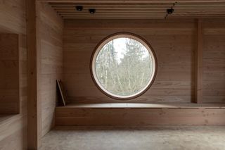 Inside, looking out through round window at House of Nature by Revaerk Arkitektur