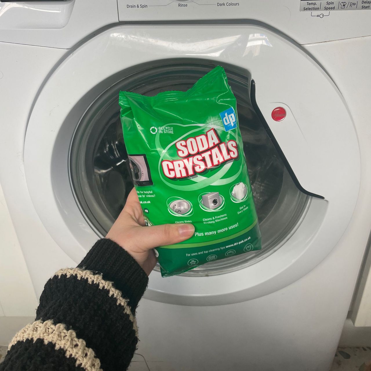 Holding a bag of soda crystals up to a white washing machine