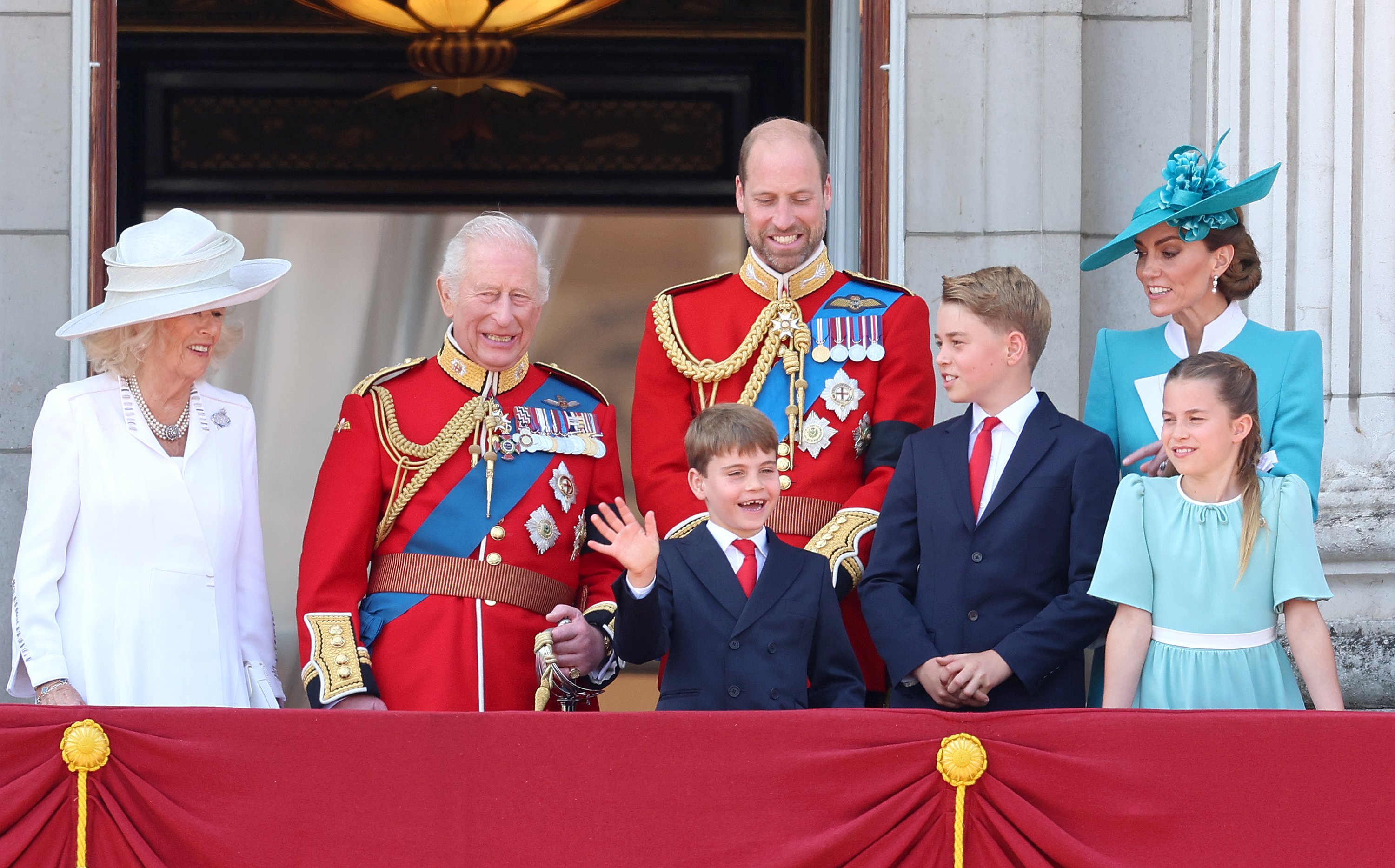 Prince Louis wears a navy suit, white shirt, and red tie at Trooping the Colour 2025