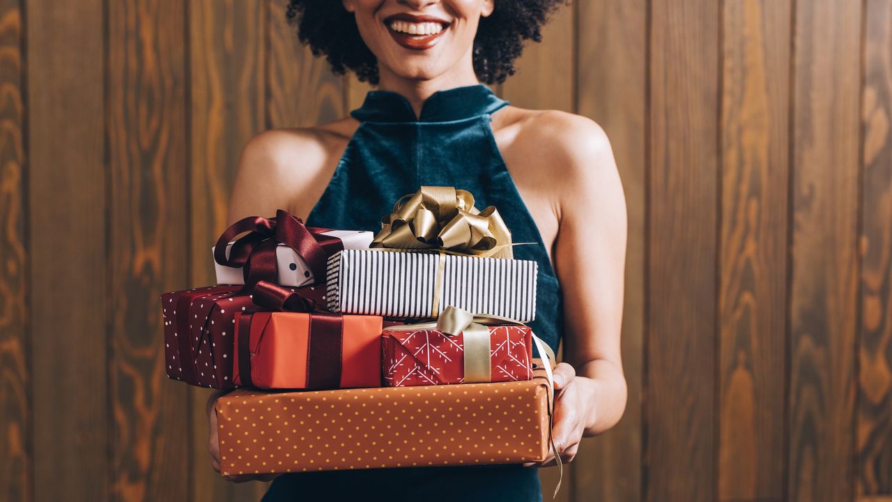 woman in halterneck velvet dress holding pile of last minute beauty gifts