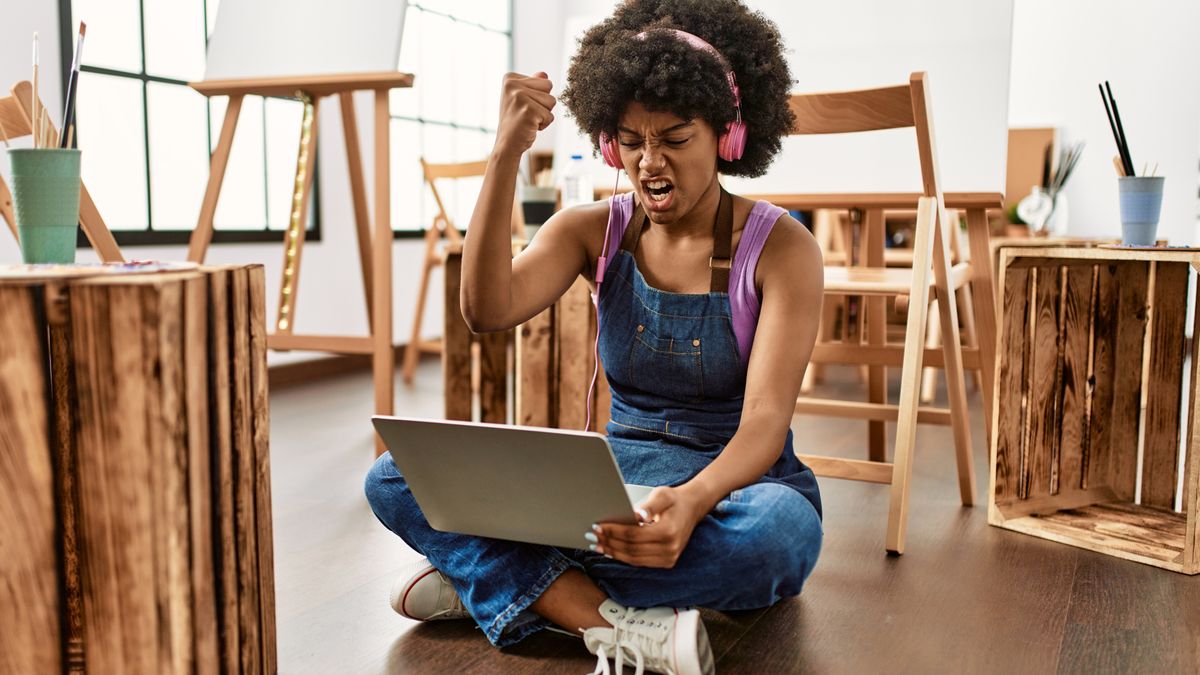 Woman in art studio using laptop annoyed and frustrated shouting with anger