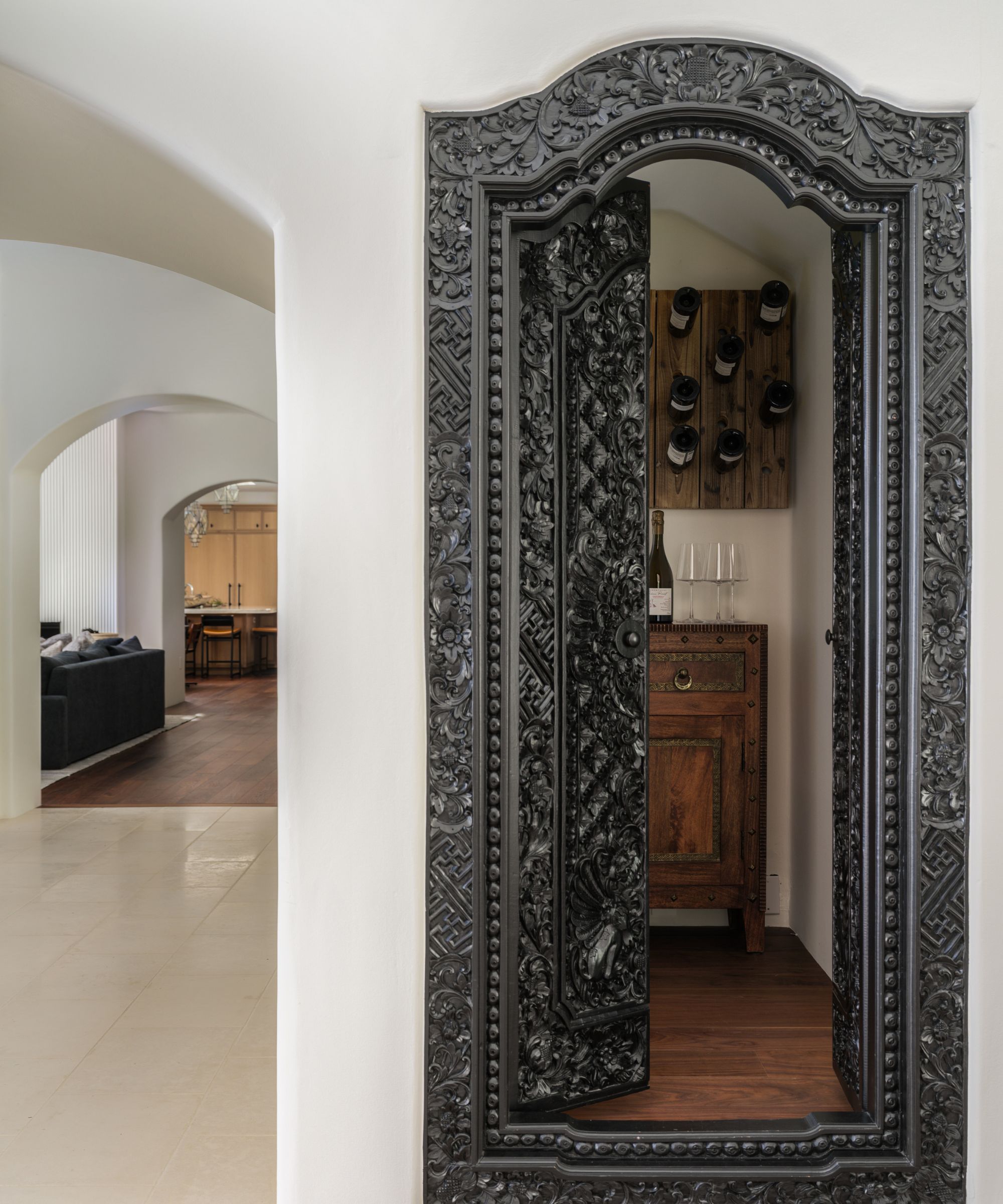 Decorative metal door leading into a small wine room, arched doorway to the side leading out to open-plan living and dining area