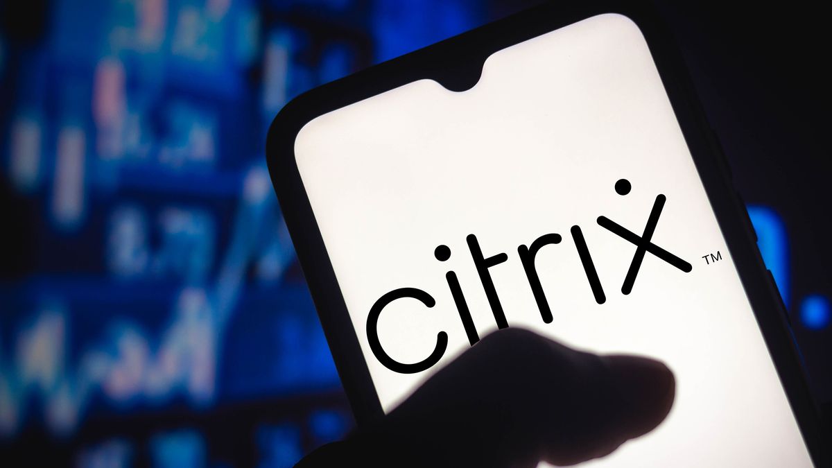 A phone showing the Citrix logo in black against a white background. It is held in the hand of an unseen person, with blurred blue stock graphs in the background.