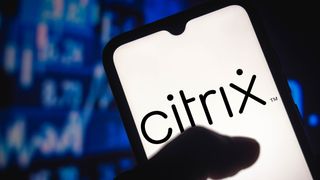 A phone showing the Citrix logo in black against a white background. It is held in the hand of an unseen person, with blurred blue stock graphs in the background.