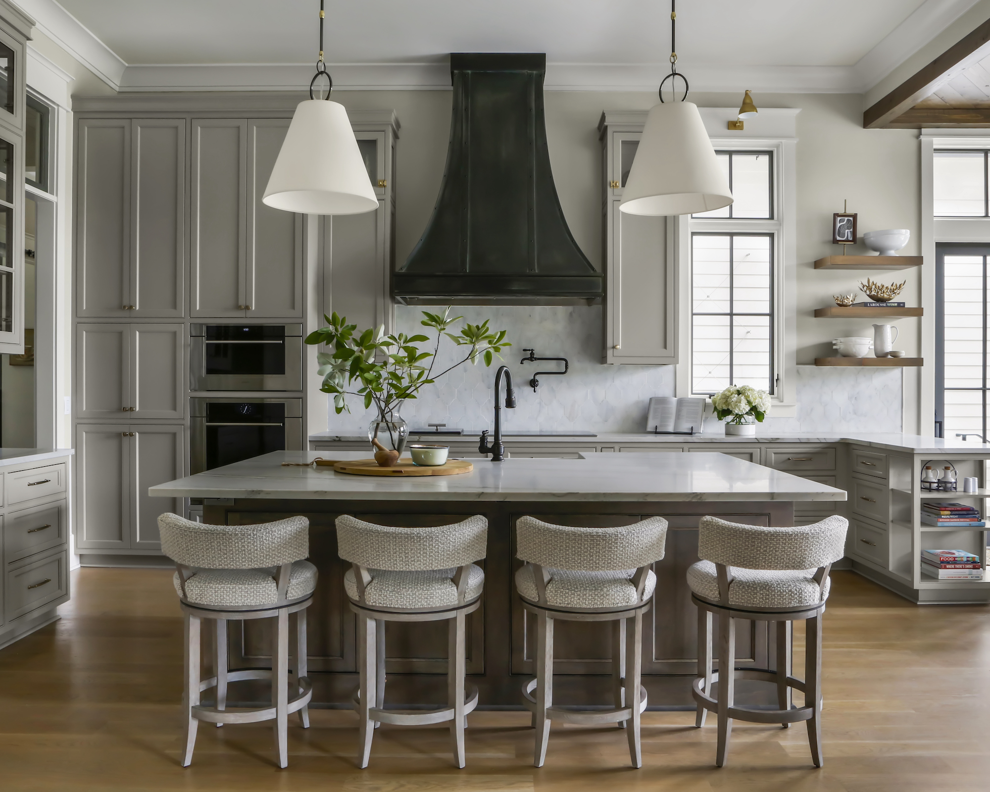 Kitchen with warm gray cabinets, island with four barstools with pendant lights over and black faucets