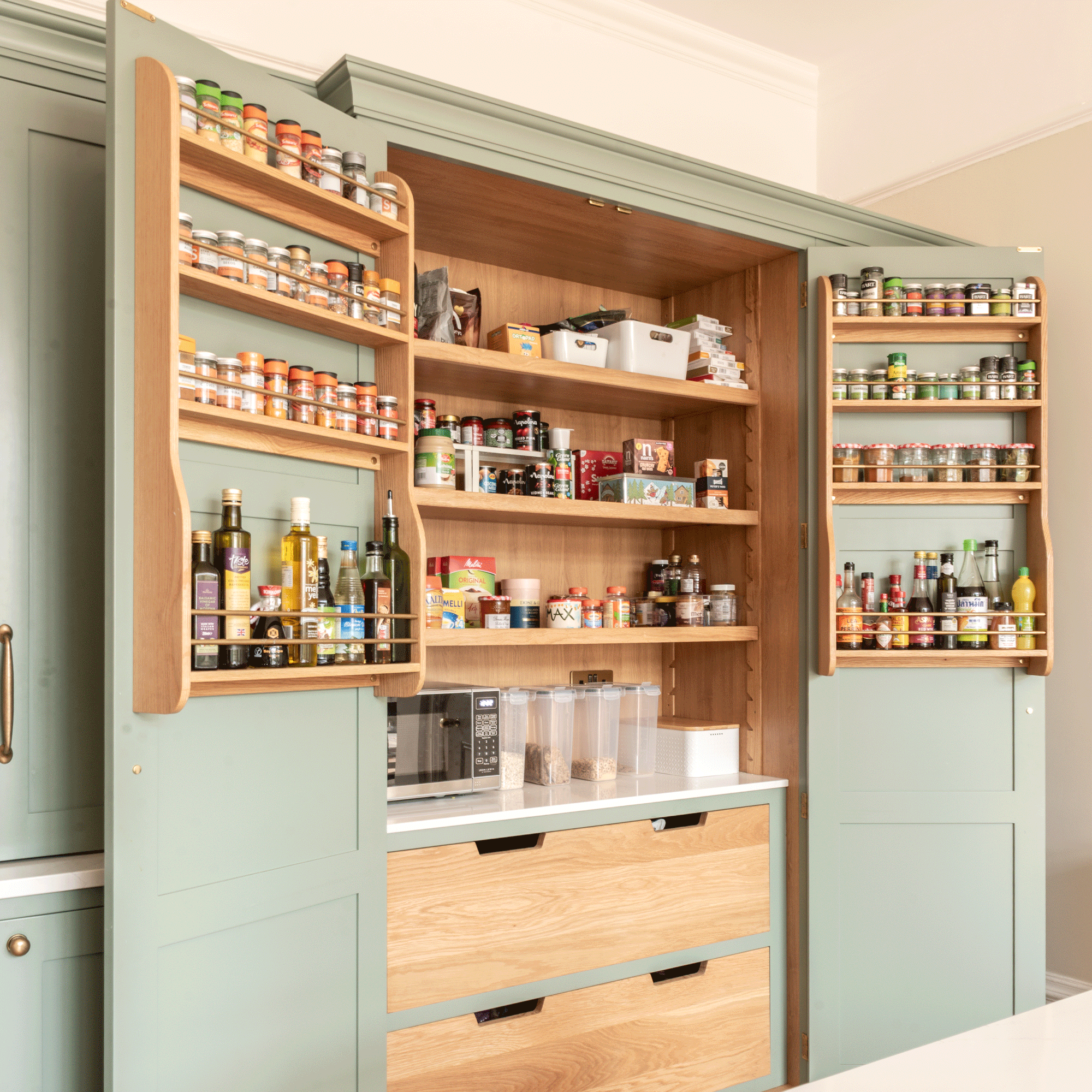 a kitchen with sage green cabinets and a a pantry cupboard packed with shelving and drawers