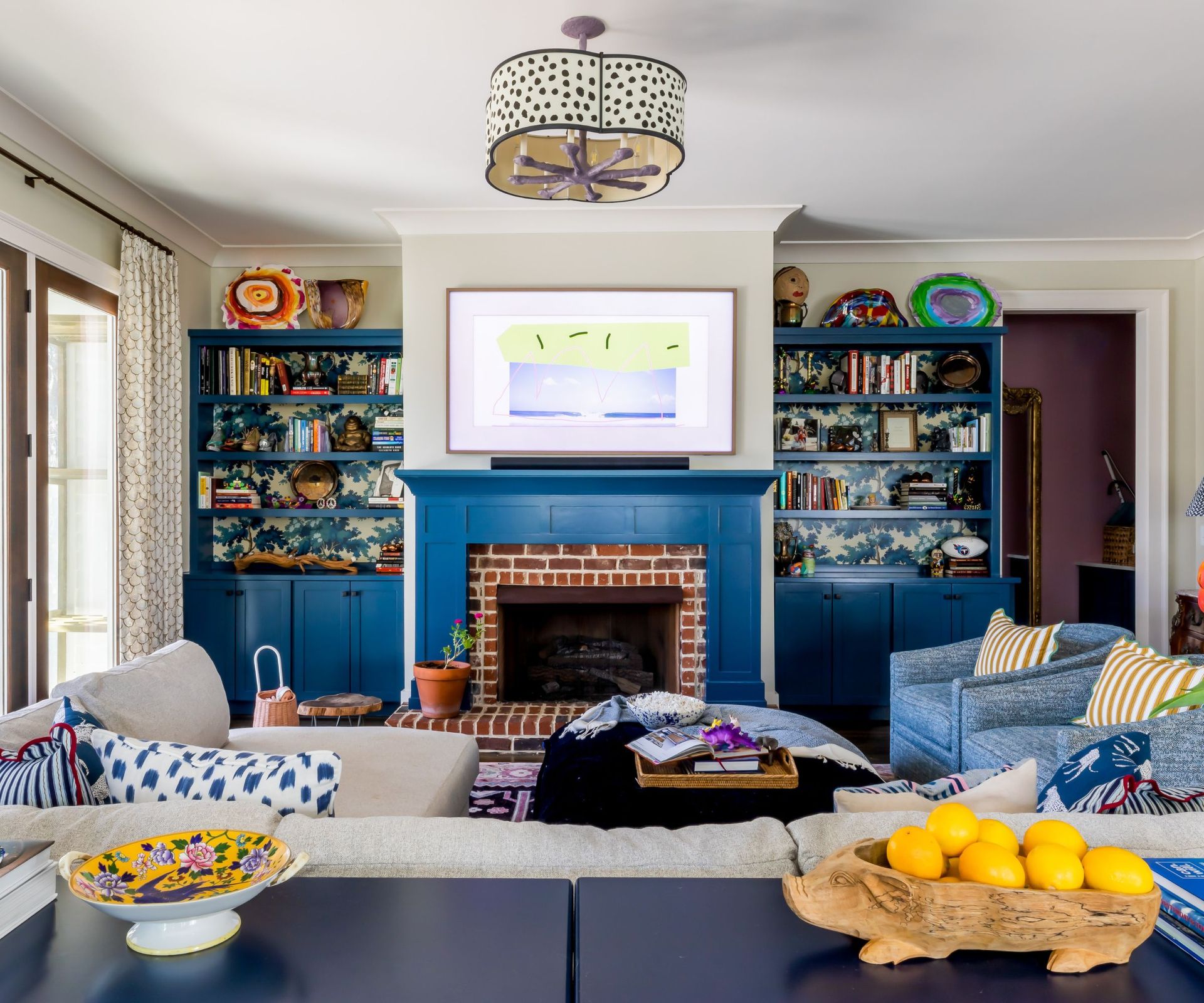 Living room with blue fireplace, sofas with stripe and polka dot cushions, shelves with wallpaper and fruit bowl with lemons