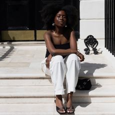 @daniellejinadu wears a pair of mule sandals with white trousers and a black bandeau top