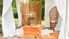 Pretty patio with boho orange and white tassled soft furnishings under a billowing white curtain canopy