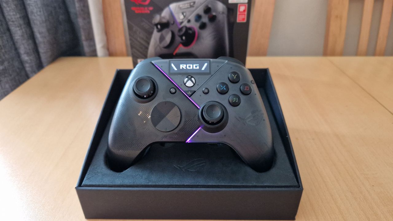 Asus ROG Raikiri Pro standing upright in its box with pink LED lights on and its OLED display showing the ROG logo