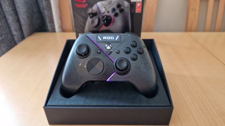 Asus ROG Raikiri Pro standing upright in its box with pink LED lights on and its OLED display showing the ROG logo