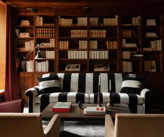 A built in fll wall oak bockcase behind a black and white striped sofa