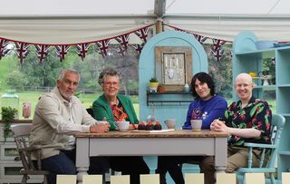 Matt Lucas, Noel Fielding and The Great British Bake Off judges sitting around a table 
