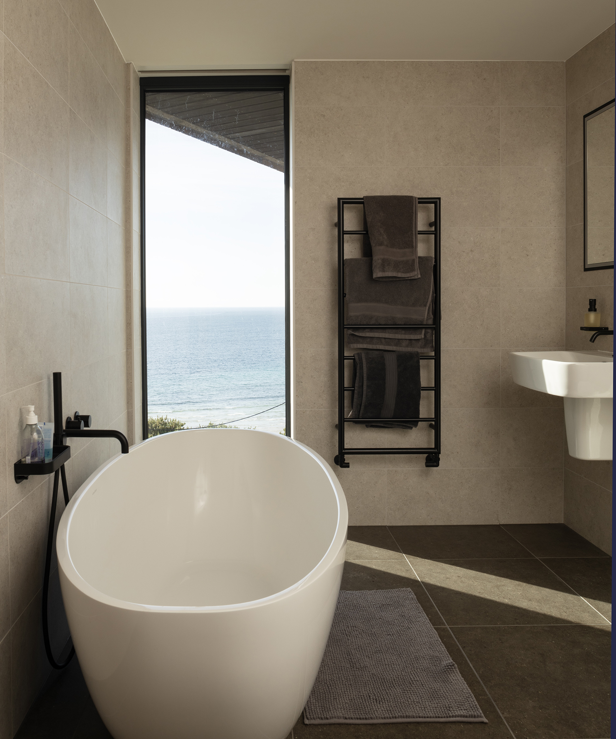 A bathroom in. anew build home with neutral decor and vertical picture window with sea view