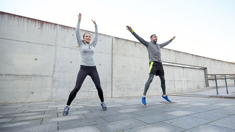 Man and a woman doing jumping jacks outside