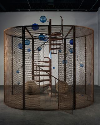 A cylinder shape cage featuring hanging balls and a staircase.